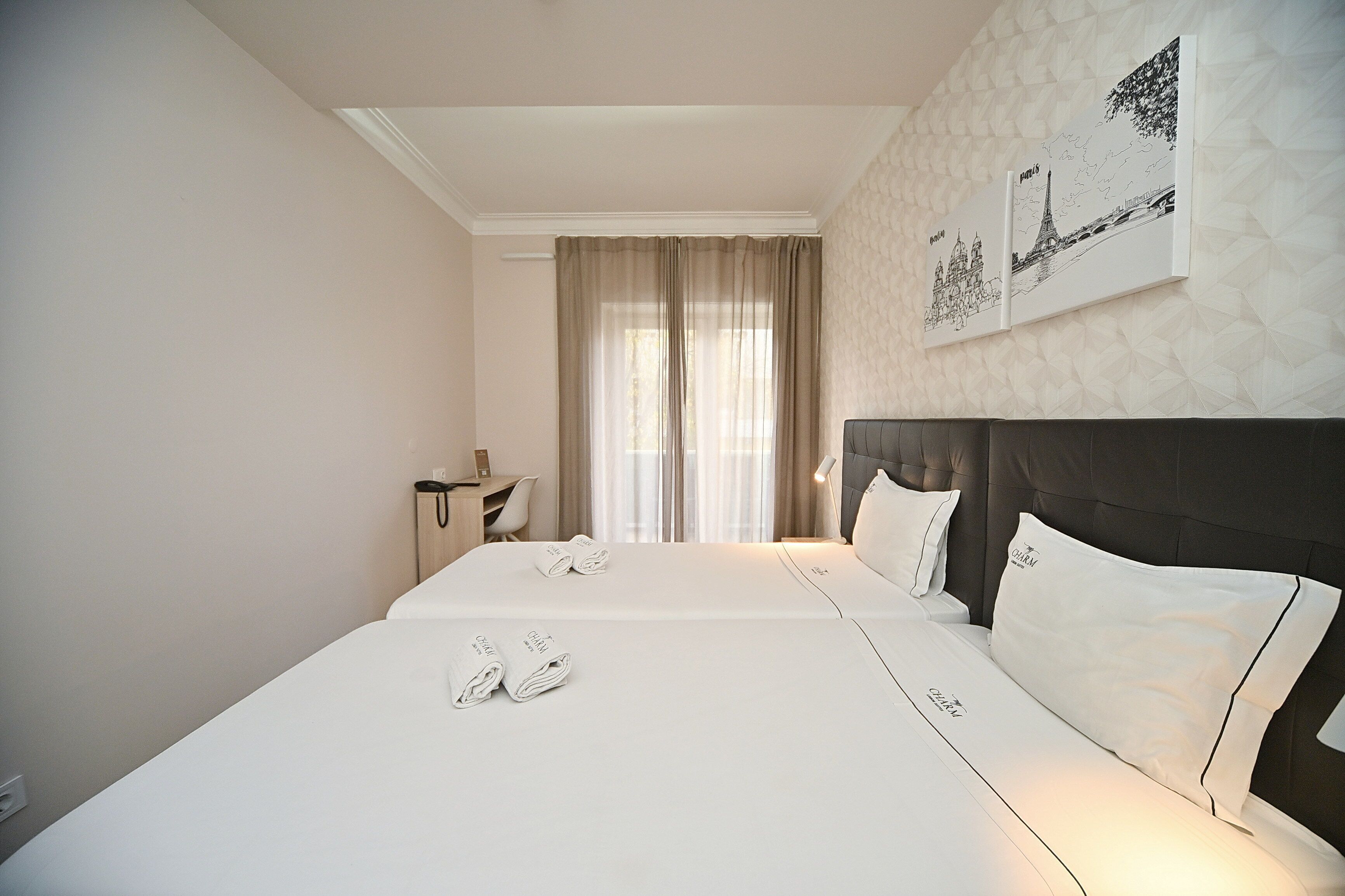 Ein Hotelzimmer mit zwei Betten, einem Schreibtisch und einem großen Fenster mit Vorhängen.