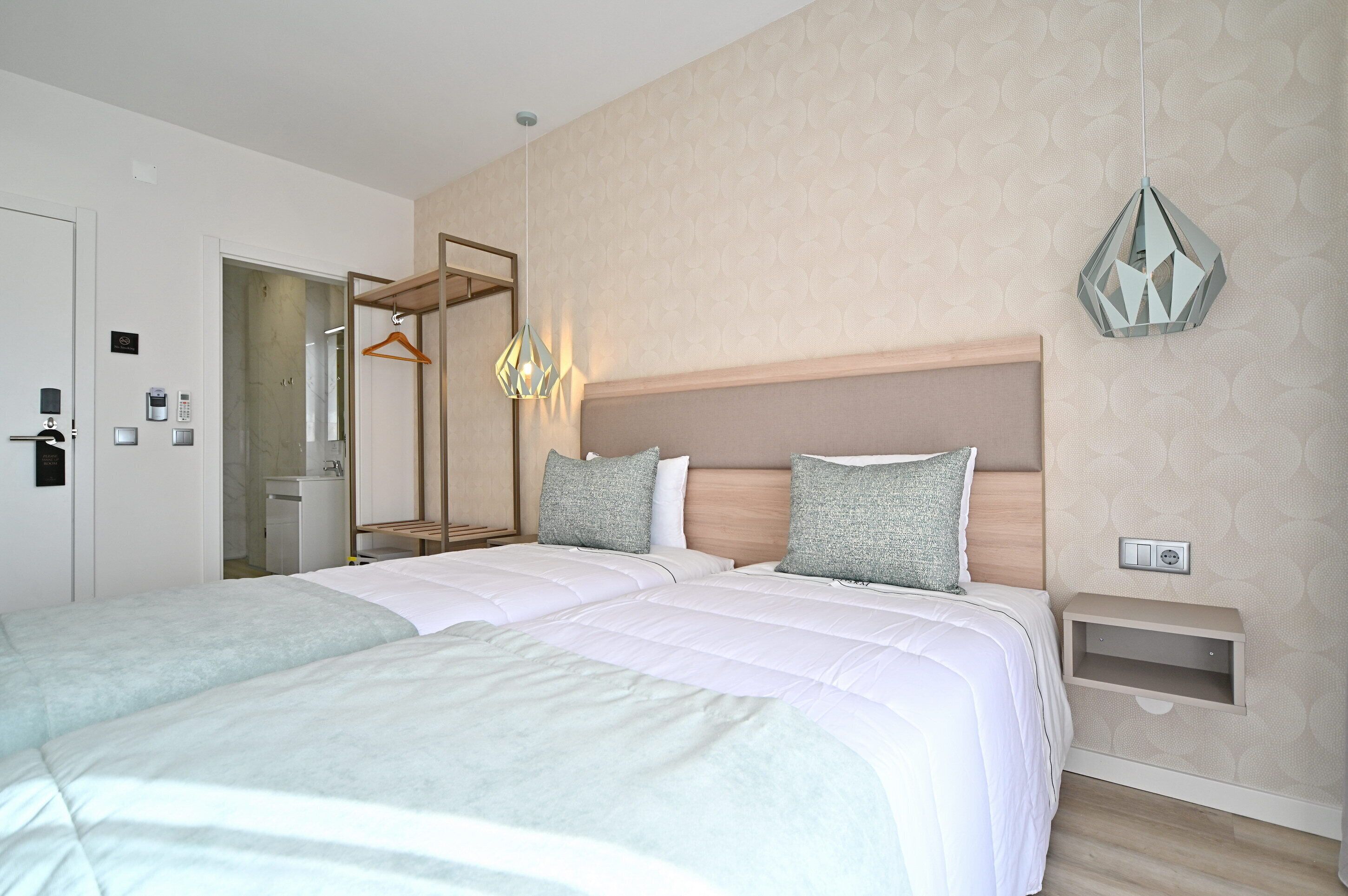 Een moderne hotelkamer met twee bedden, een houten hoofdbord, een hanglamp en een klein nachtkastje.