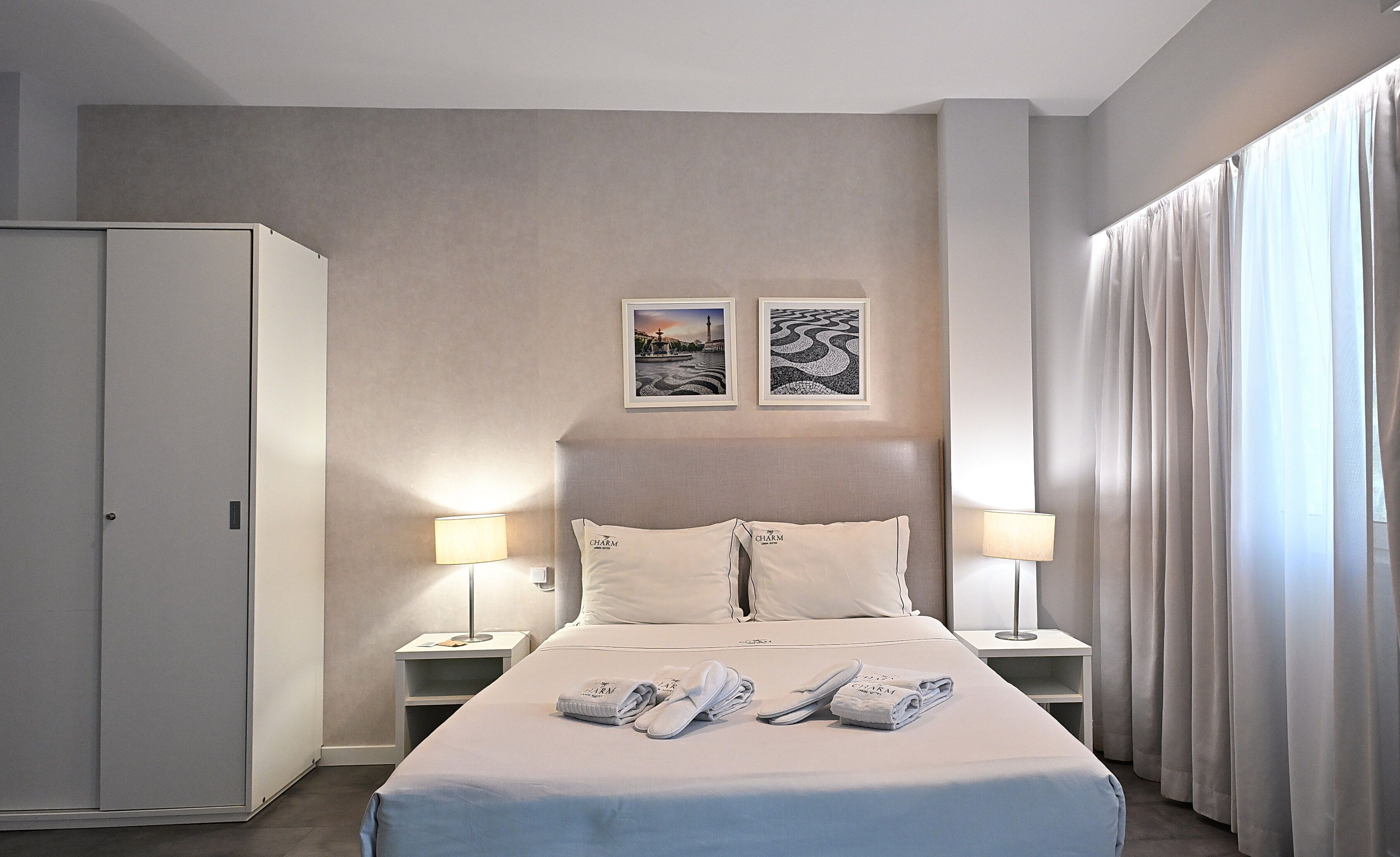 Een hotelkamer met een bed, twee bedlampen, een kledingkast en twee ingelijste foto's aan de muur.