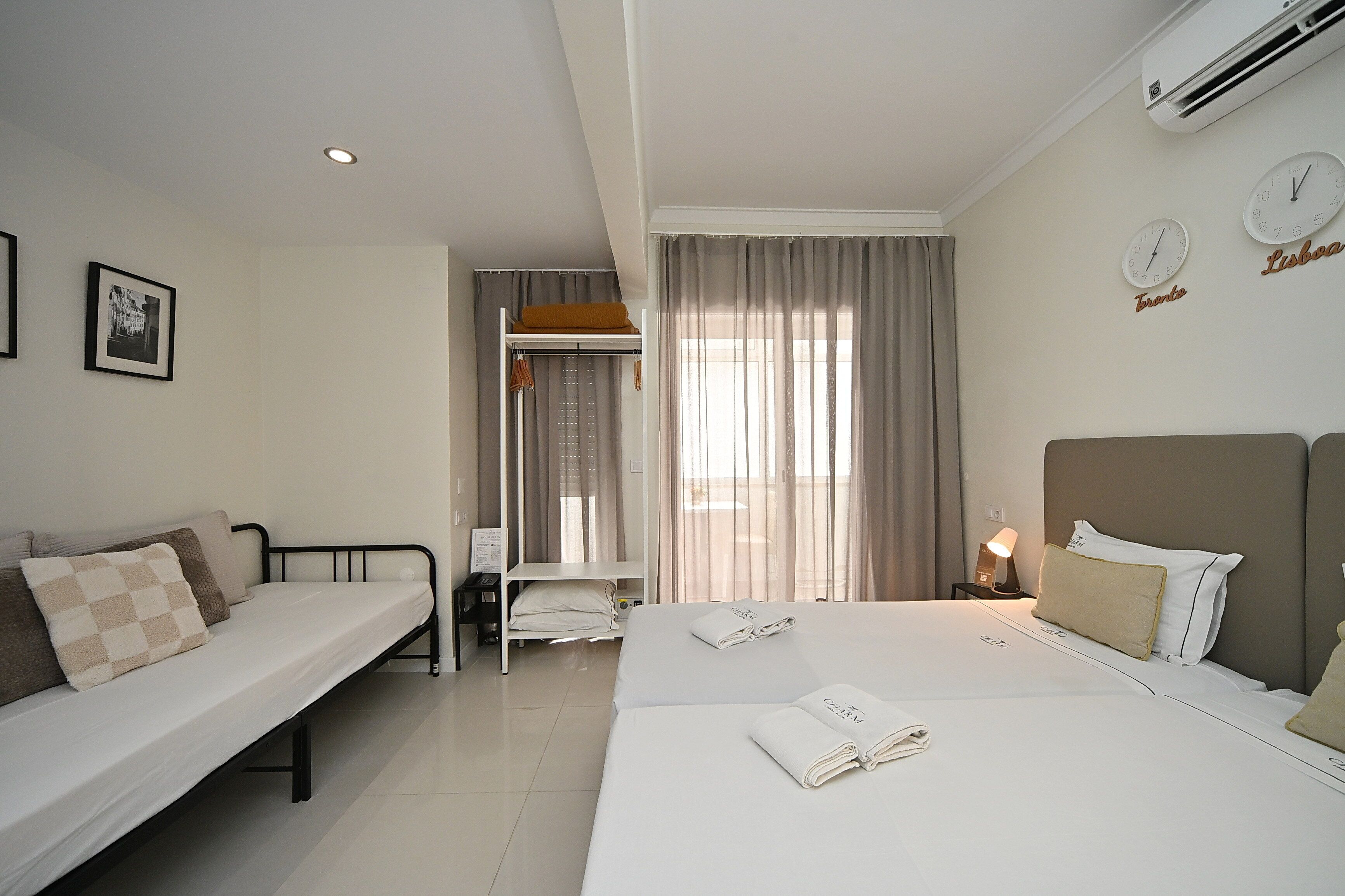Quarto de hotel com cama, sofá, escrivaninha e janela com cortinas.