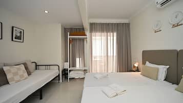 Quarto de hotel com cama, sofá, escrivaninha e janela com cortinas.