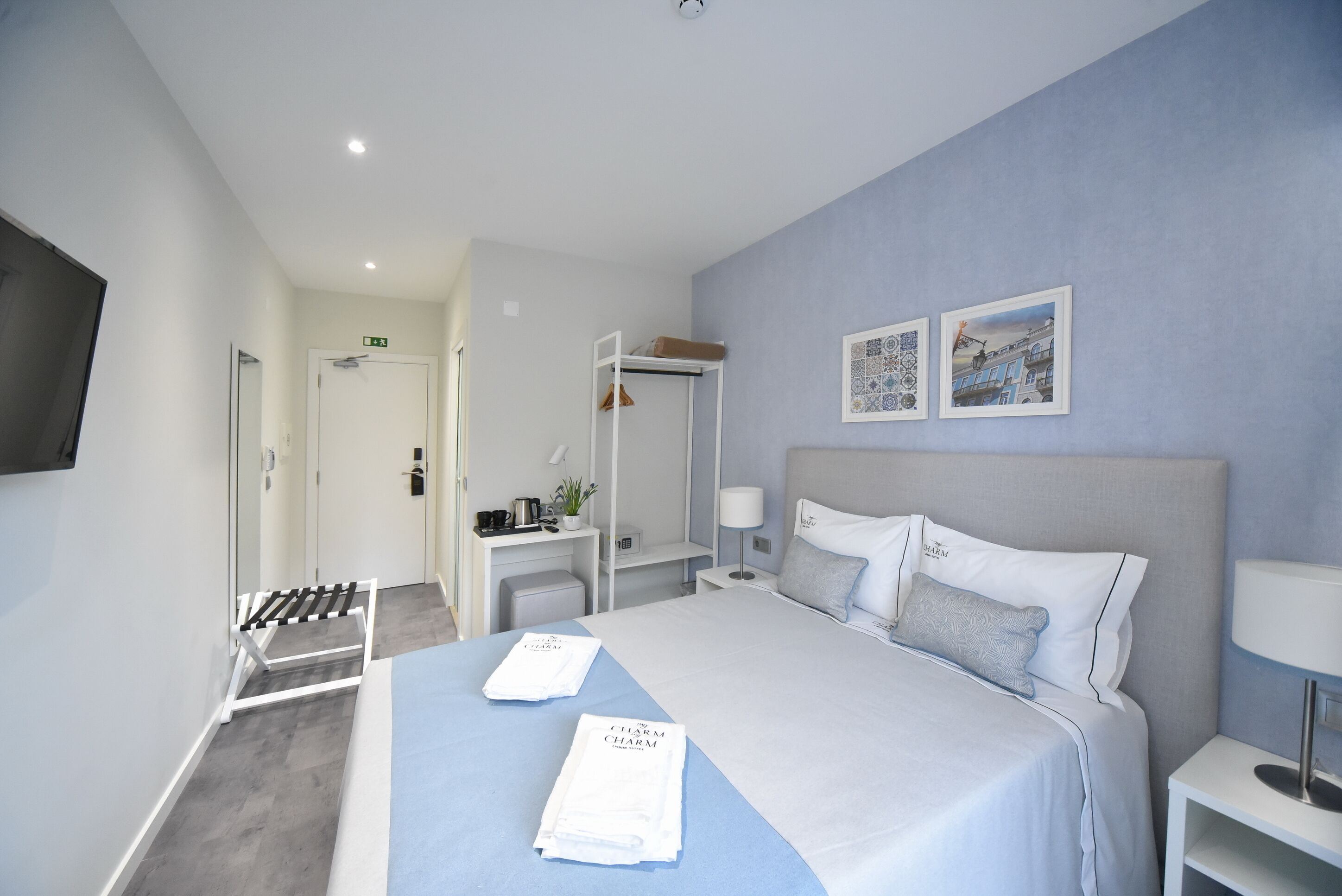 A modern hotel room with a large bed, a desk, a chair, a TV, and artwork on the wall.