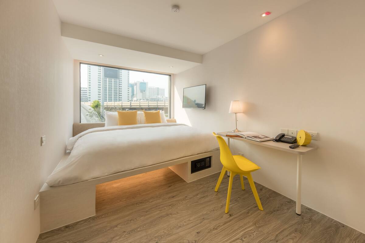Een moderne hotelkamer met een bed, een bureau, een stoel, een televisie en een raam met uitzicht op de stad.