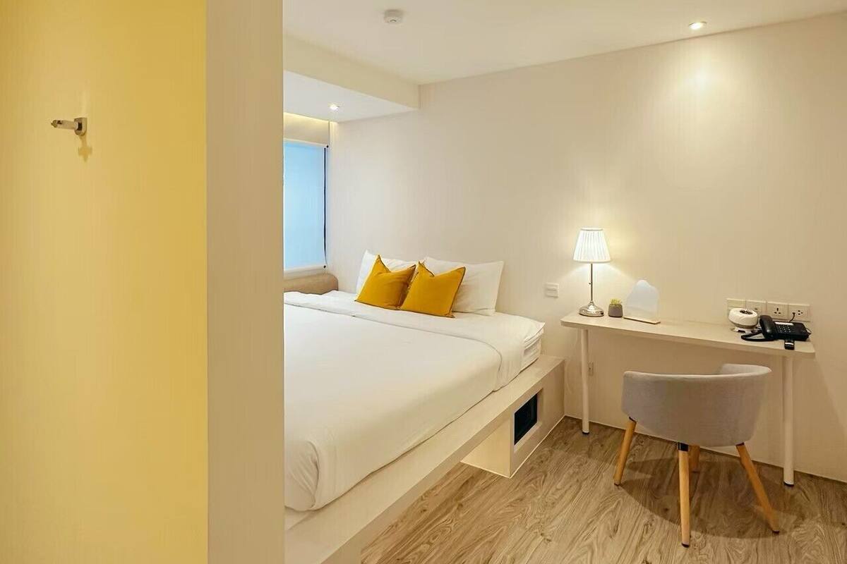 Een moderne hotelkamer met een bed, nachtkastje, lamp en een bureau met stoel.