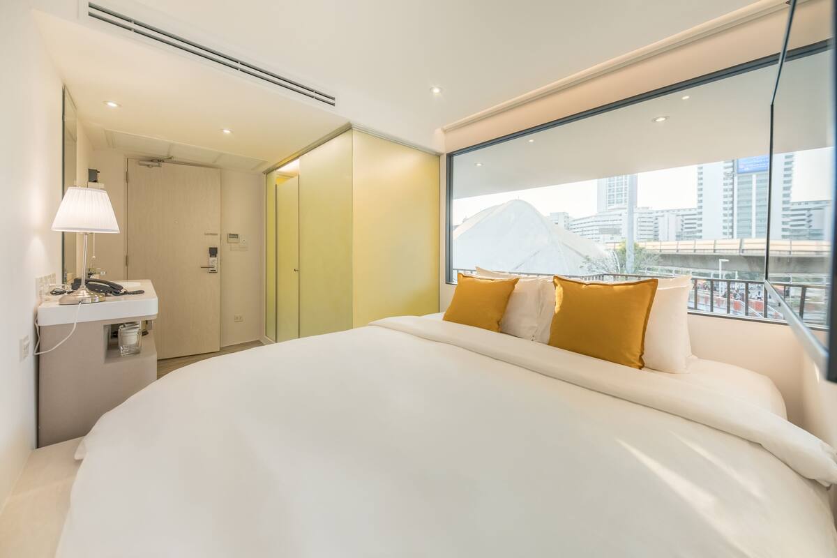 Een moderne hotelkamer met een groot bed, een nachtkastje met een lamp en een raam met uitzicht op de stad.