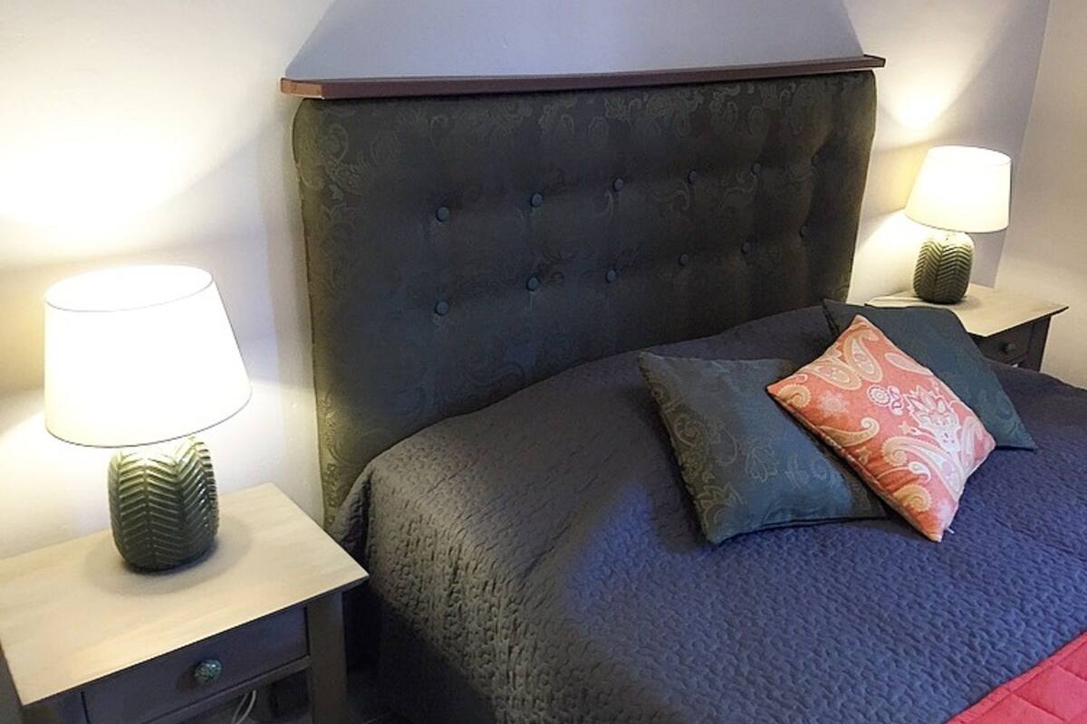 A neatly arranged bedroom with a tufted headboard, a bed with a dark cover, two bedside lamps, and a nightstand with a drawer.