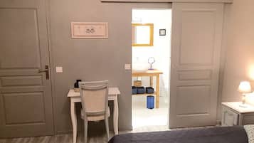Un dormitorio con una cama, un escritorio y una silla. Se ve un baño a través de una puerta abierta.