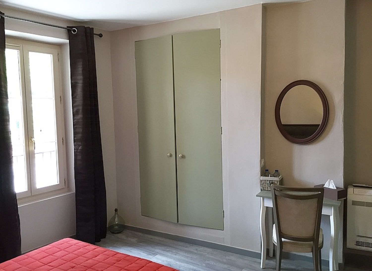 Ein Schlafzimmer mit einem Bett, einem Kleiderschrank, einem Schreibtisch mit Stuhl, einem Spiegel und einem Fenster mit Vorhängen.