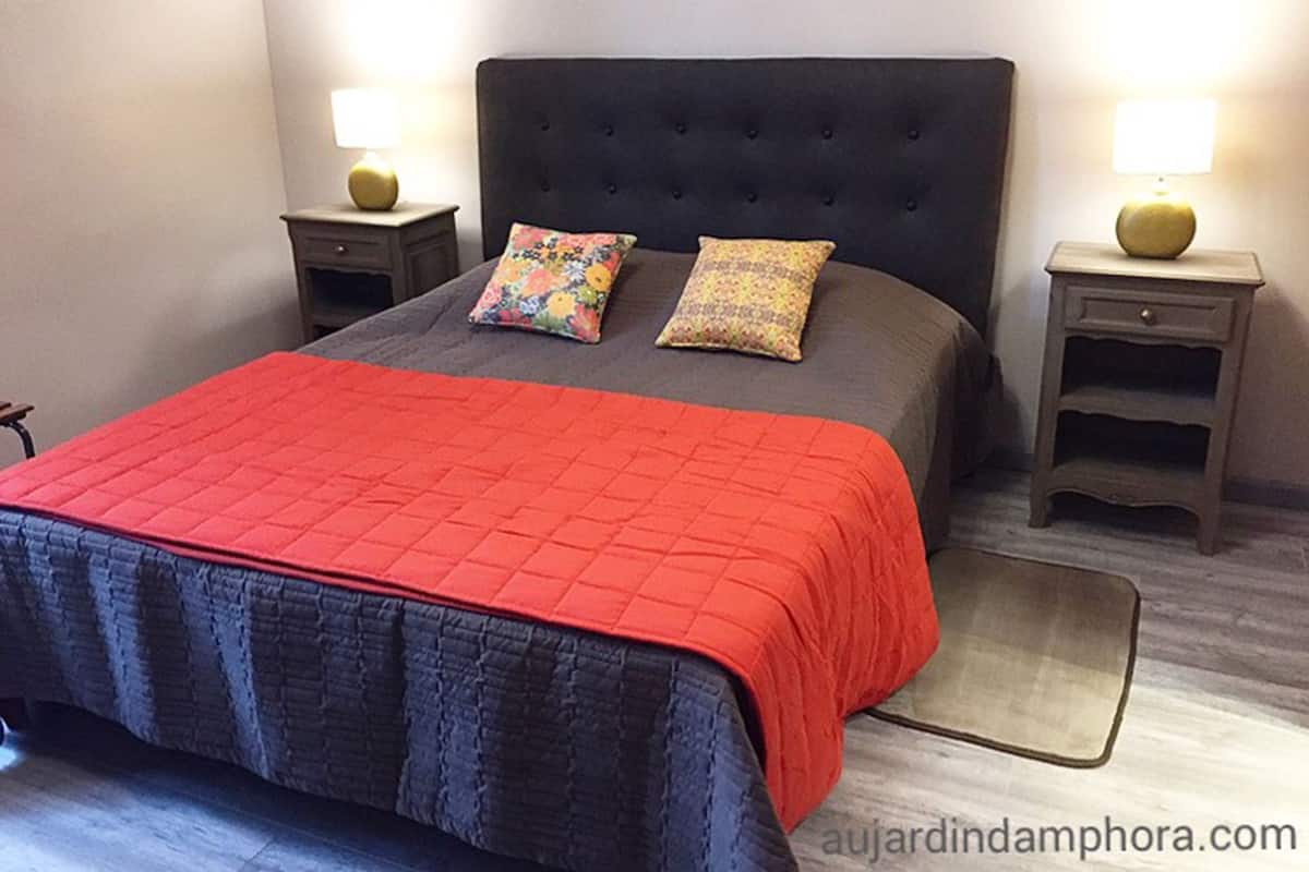 A neatly made bed with a red blanket and two pillows, flanked by two bedside tables with lamps.