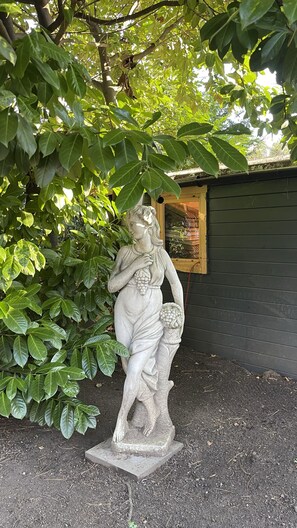 A stone statue of a woman holding a basket of grapes, surrounded by lush green foliage. - Hotel Haus Gimken (Essen)