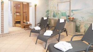 A spa room with three chairs, a wooden cabinet with a bowl of fruit, and a mural on the wall. - Hotel Haus Gimken (Essen)