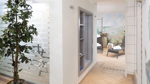 A hallway with a potted plant, a glass partition, a door leading to a room with a bed and a chair, and a mural on the wall. - Hotel Haus Gimken (Essen)