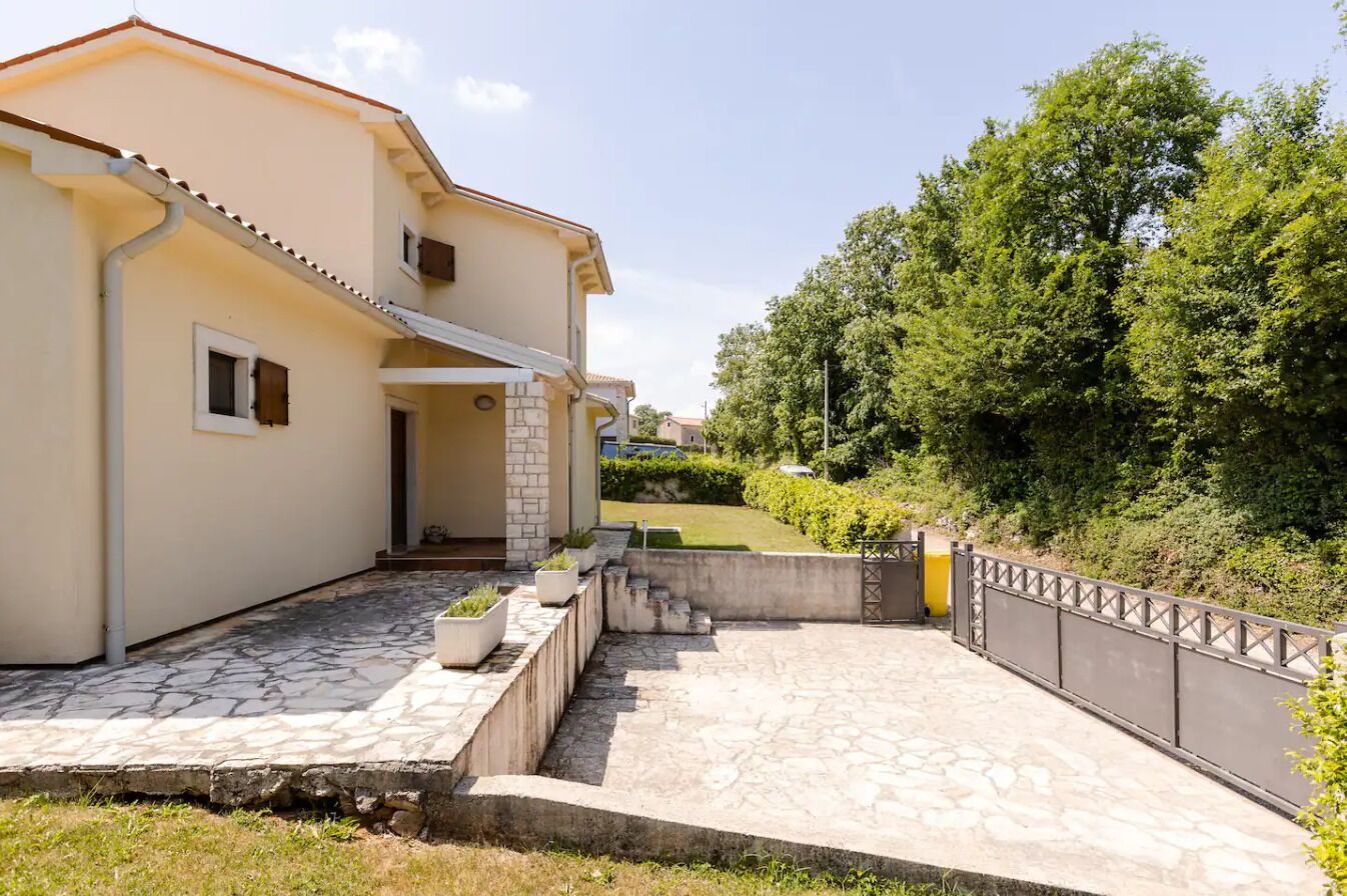 A two-story house with a stone patio, a small garden, and a metal fence.