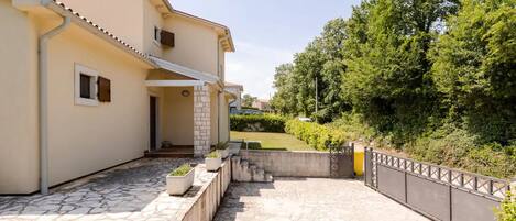 A two-story house with a stone patio, a small garden, and a metal fence.