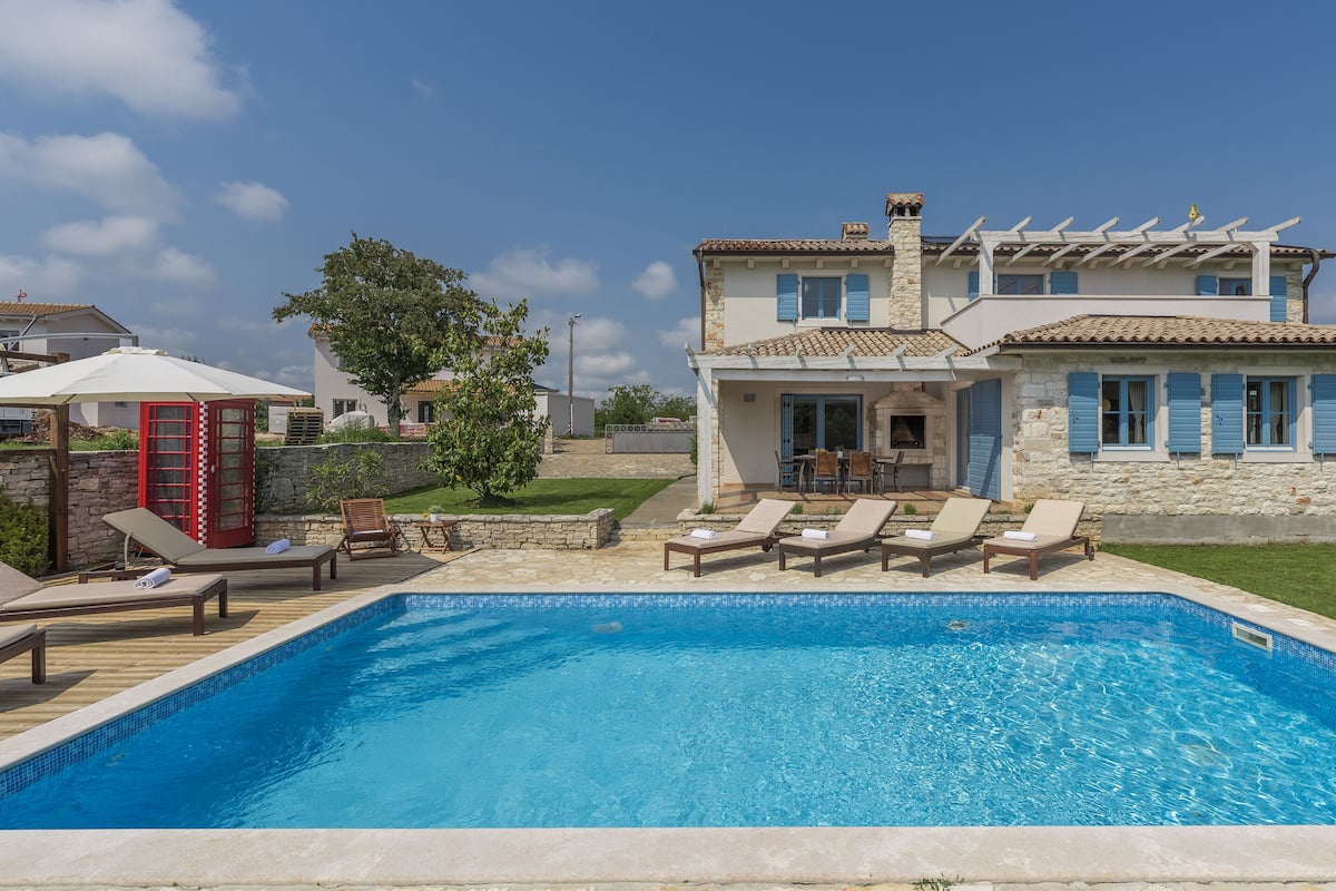 A two-story house with a swimming pool, outdoor seating, and a stone facade.