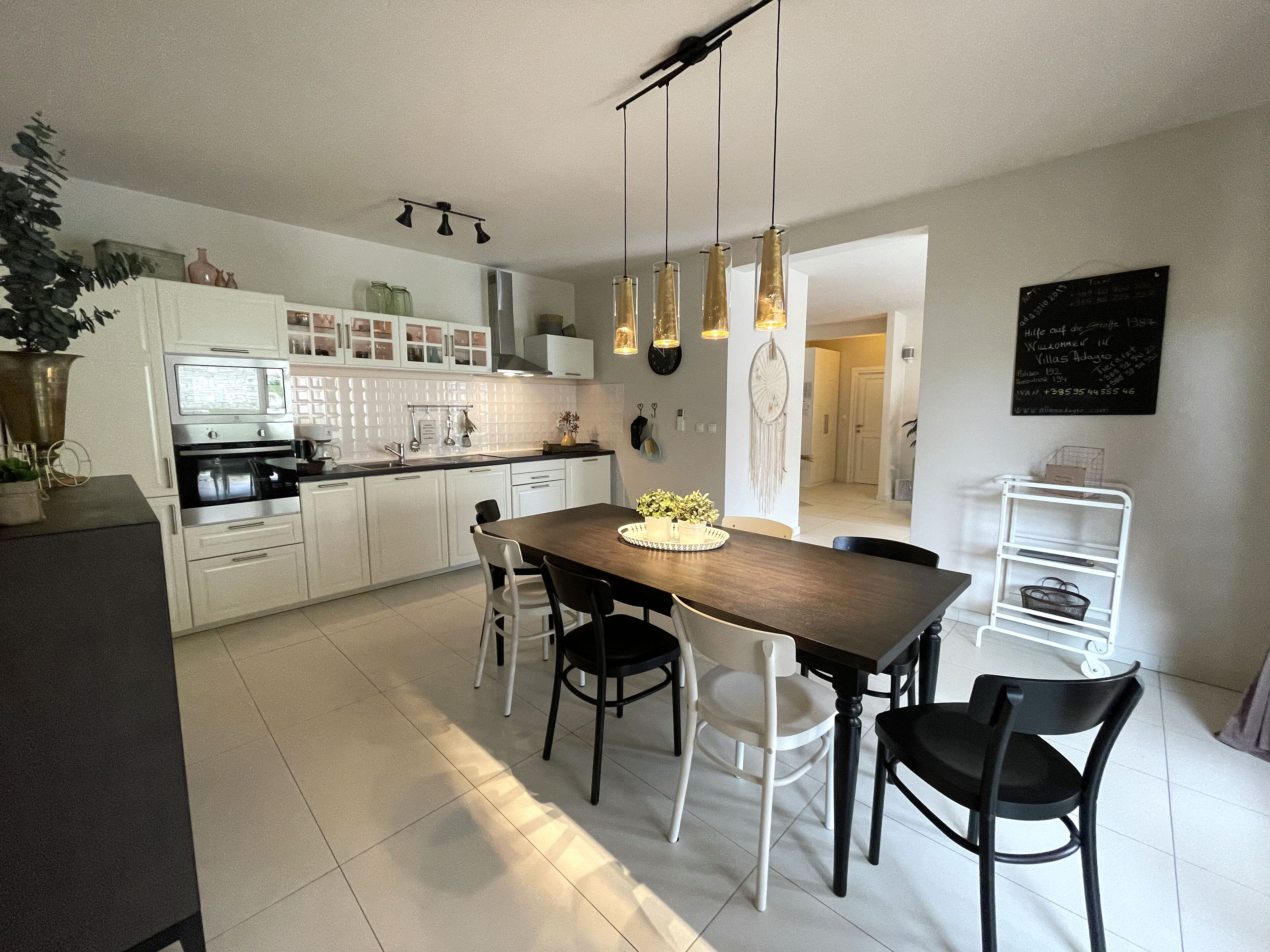 A modern kitchen with white cabinets, a wooden dining table, and pendant lights.