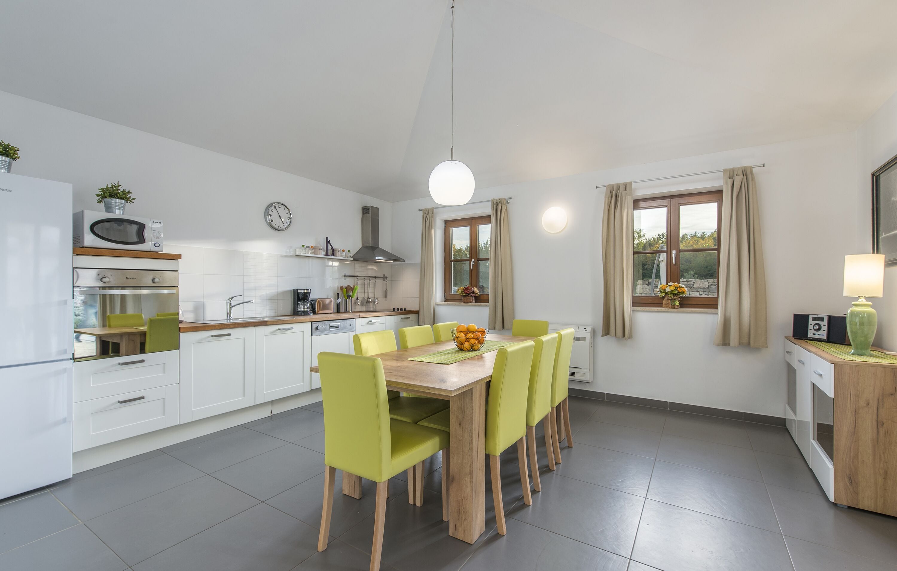 Une cuisine moderne avec des meubles blancs, une table à manger en bois et des chaises vertes.