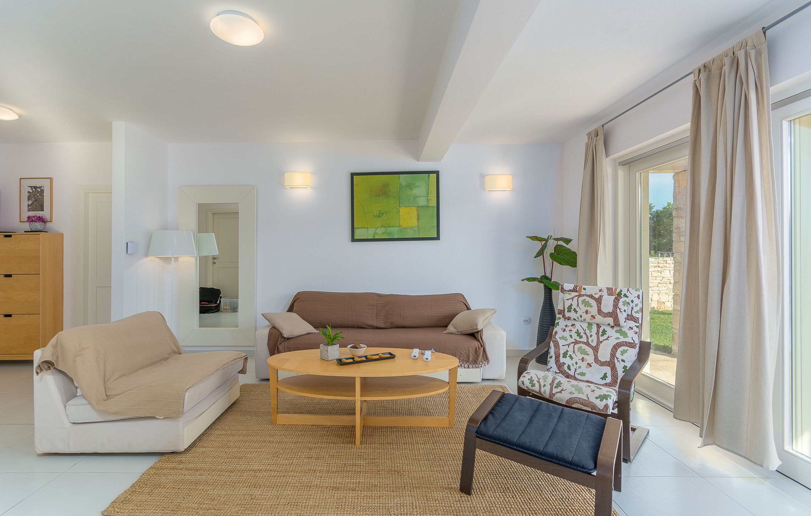 A modern living room with a sofa, armchair, and coffee table. There is a painting on the wall and a window with curtains.