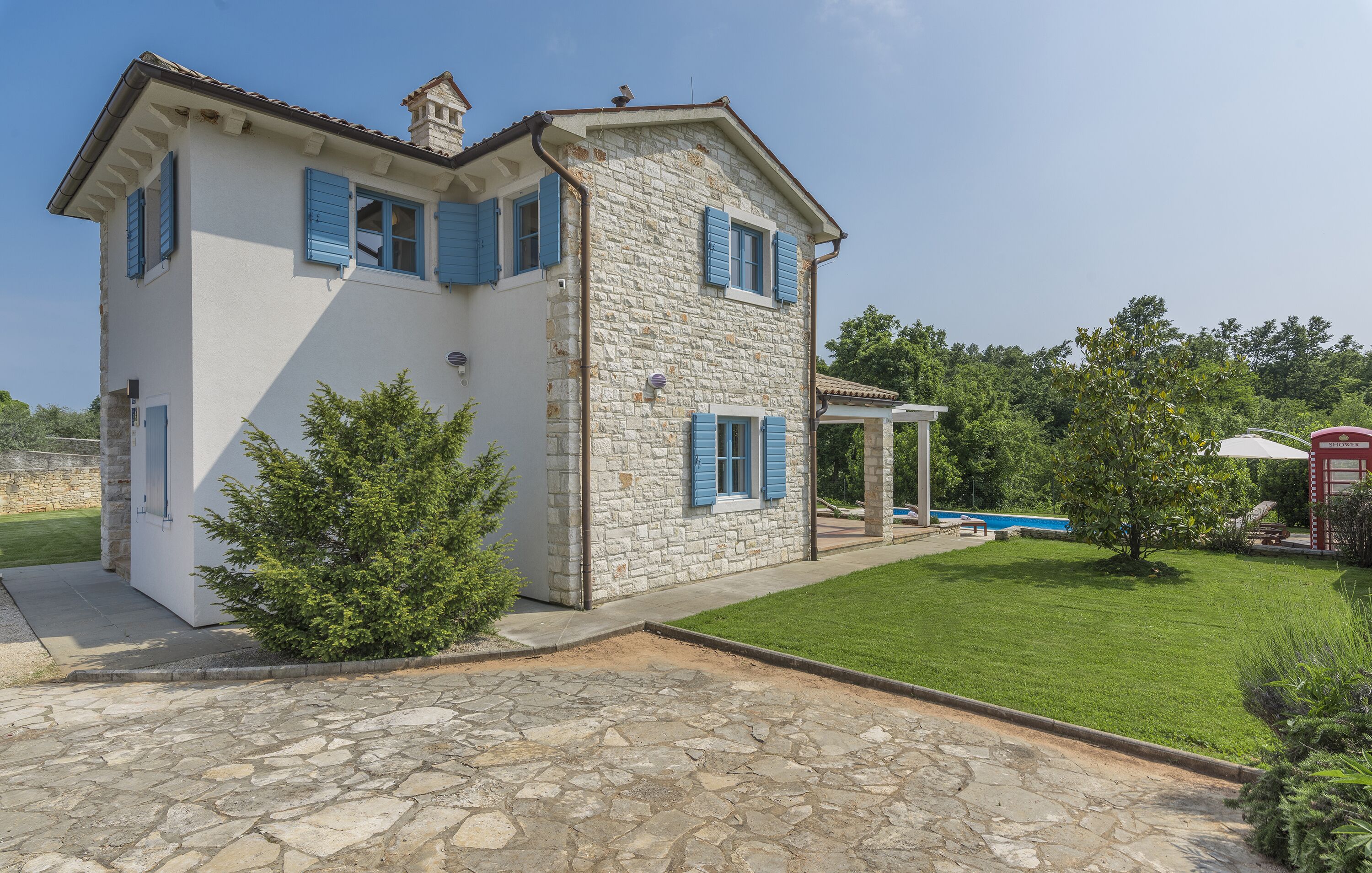 A two-story house with stone walls and blue shutters, a stone driveway, and a well-maintained lawn.