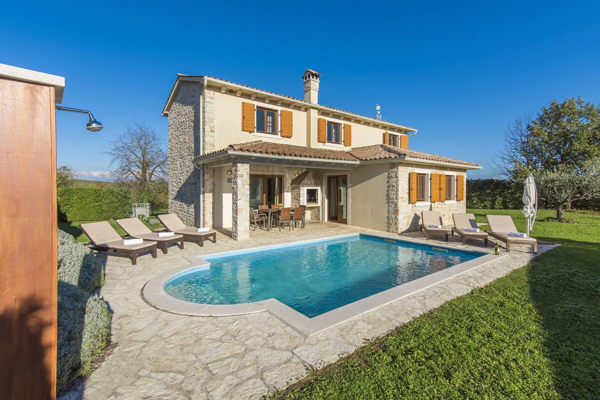 A two-story house with a swimming pool, stone exterior, and outdoor seating area.