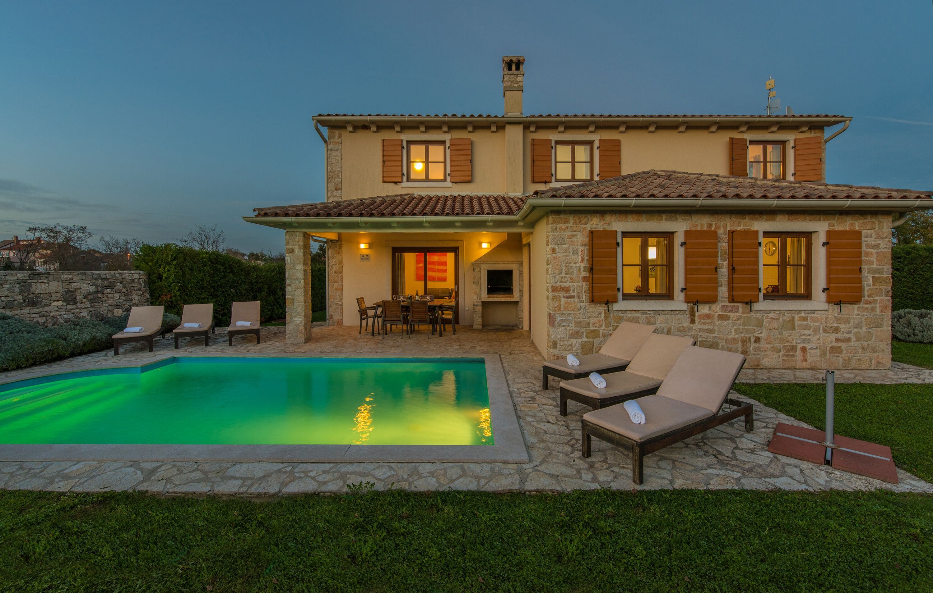 Une maison à deux étages avec une piscine, un espace salon extérieur et des murs en pierre.
