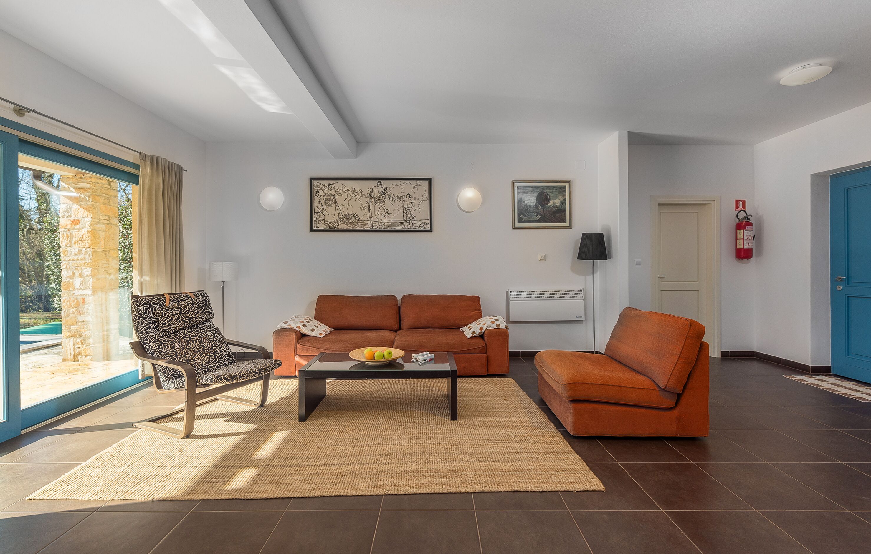 Uma sala de estar com sofá, poltrona, mesa de centro e vista para o exterior.