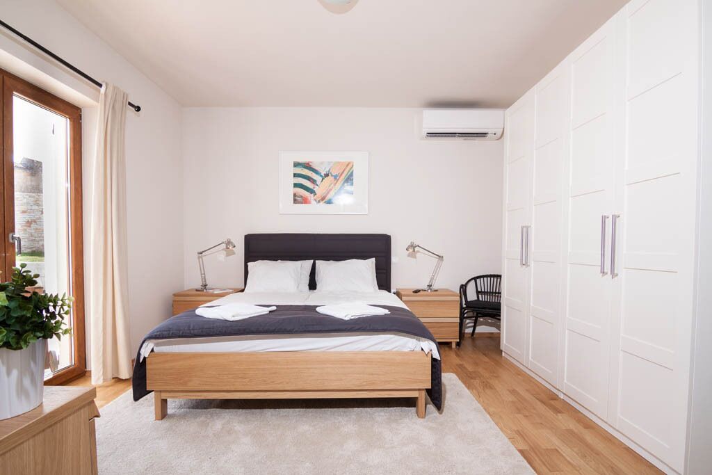A bedroom with a bed, bedside tables, a desk, a chair, a wardrobe, and a window with curtains.