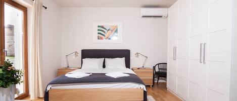 A bedroom with a bed, bedside tables, a desk, a chair, a wardrobe, and a window with curtains.