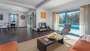 A modern living room with a glass coffee table, a TV, and a pool view. - Villas Adagio (Barban)