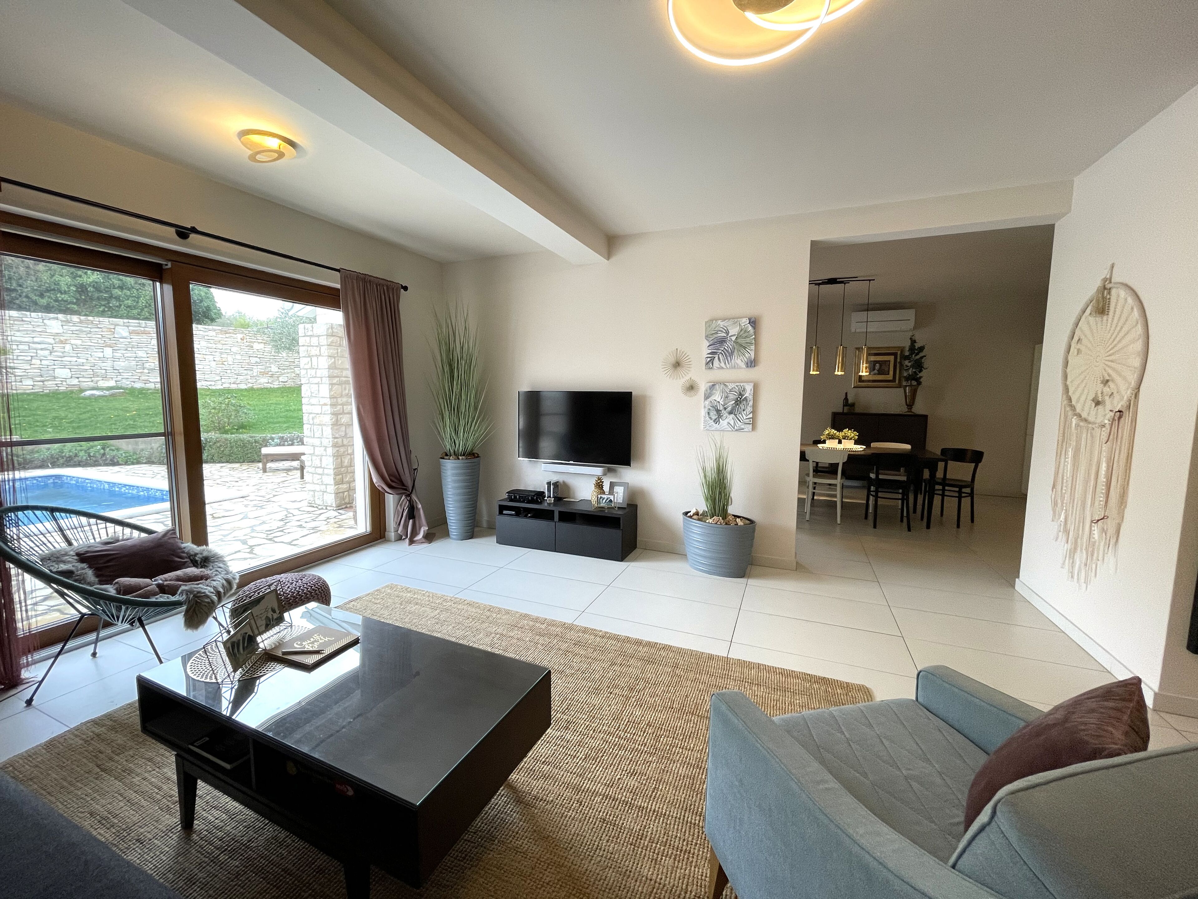 A spacious living room with a large TV, comfortable seating, a dining area, and a view of the outdoors.