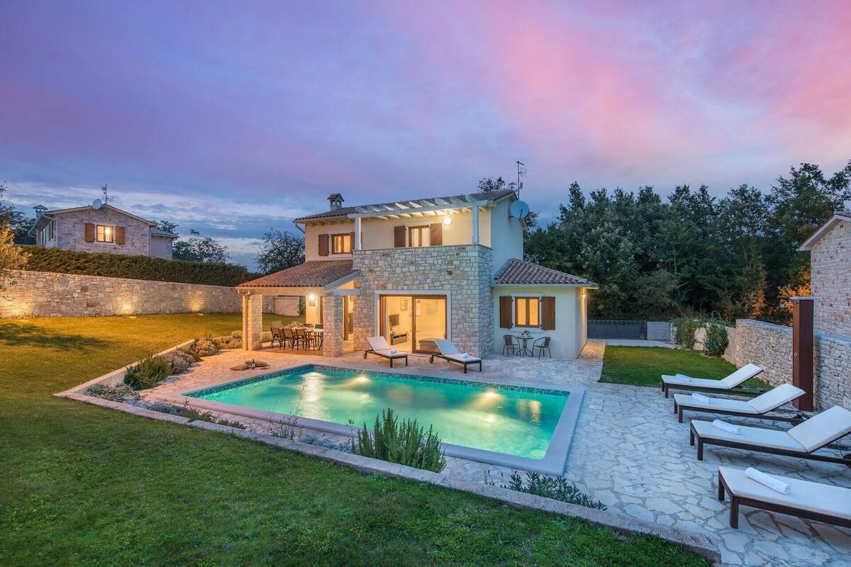 A two-story house with a stone exterior, a swimming pool, and outdoor seating.