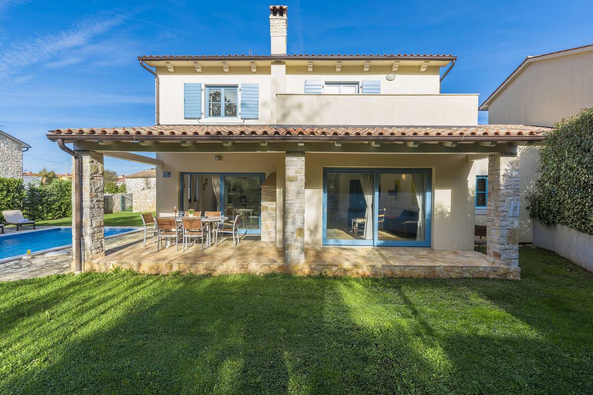 A two-story house with a swimming pool, a patio with outdoor furniture, and a stone facade.