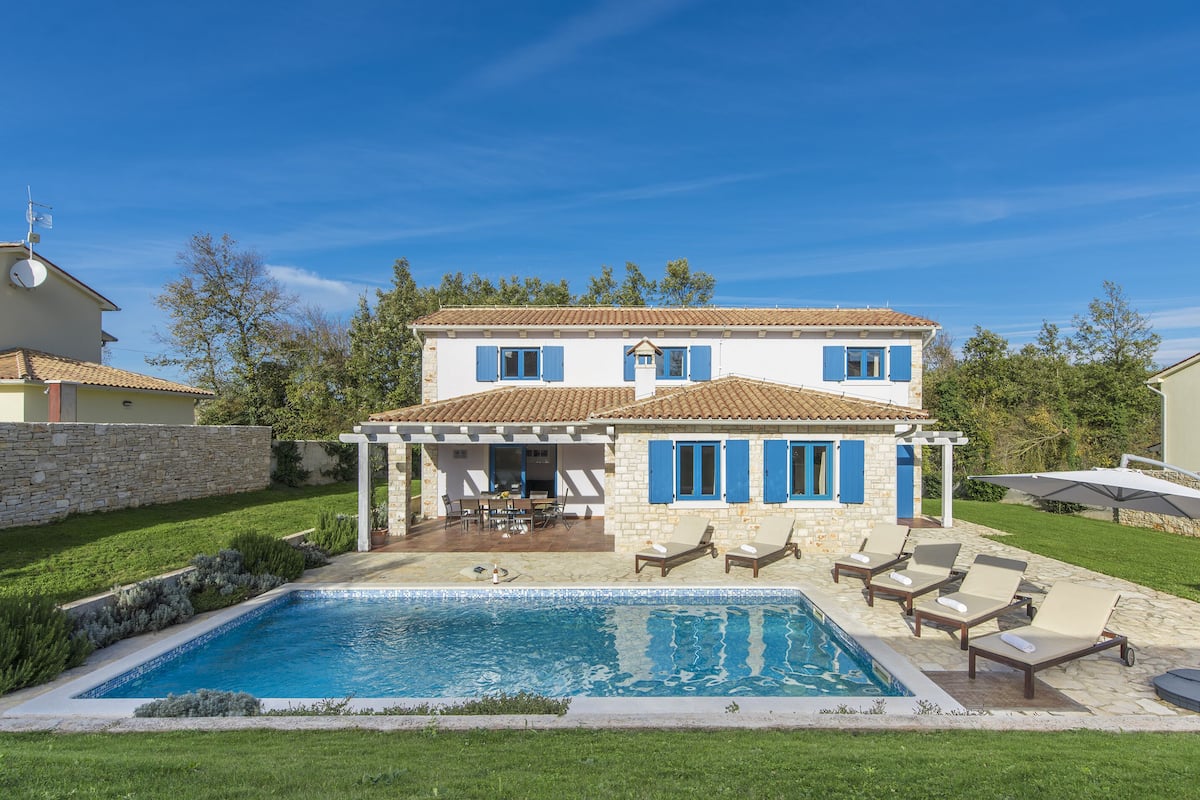 A two-story house with a swimming pool, outdoor seating, and a stone wall.