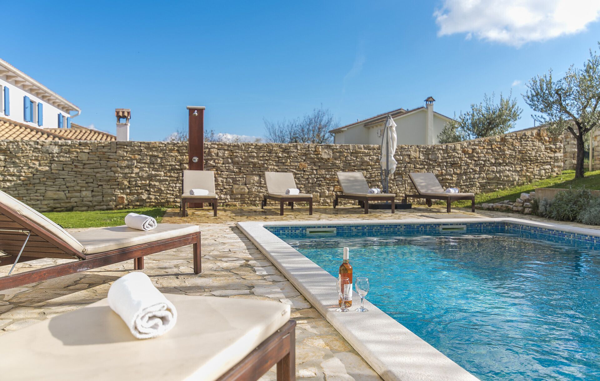 Un espace piscine avec des chaises longues, un mur en pierre et un ciel d’un bleu éclatant.