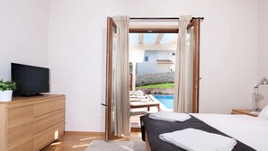 A bedroom with a bed, a TV on a wooden dresser, and a view of a swimming pool through an open door. - Villas Adagio (Barban)
