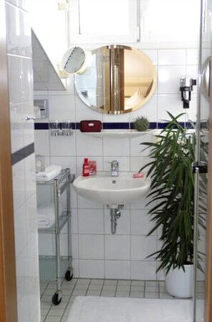 Een badkamer met een witte wastafel, een ronde spiegel, een rode zeepdispenser en een potplant.