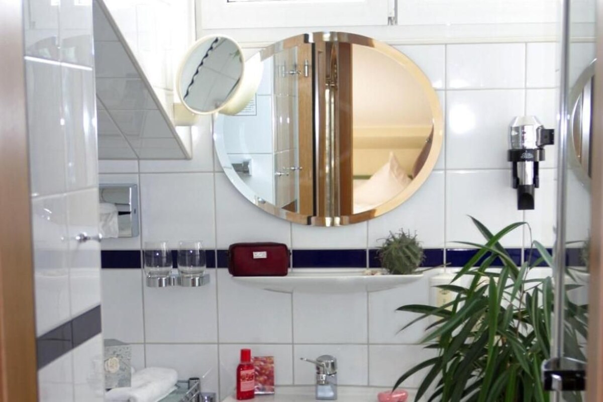 Een badkamer met een wit wastafelmeubel, een spiegel, een handdoekhouder en een kamerplant.