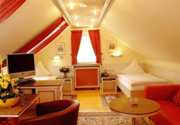 Een gezellig, goed verlichte zolderkamer met een bed, een bureau, een televisie en een rode bank.