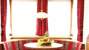 Een eetgedeelte met een ronde tafel, rode bekleden bankzit en een fruitmand op de tafel.
