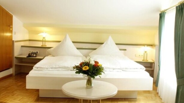 Een hotelkamer met een bed, nachtkastjes, een bloevas en een ronde tafel.