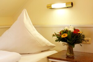 Una cama con ropa de cama blanca, un jarrón con flores y una lámpara de pared.