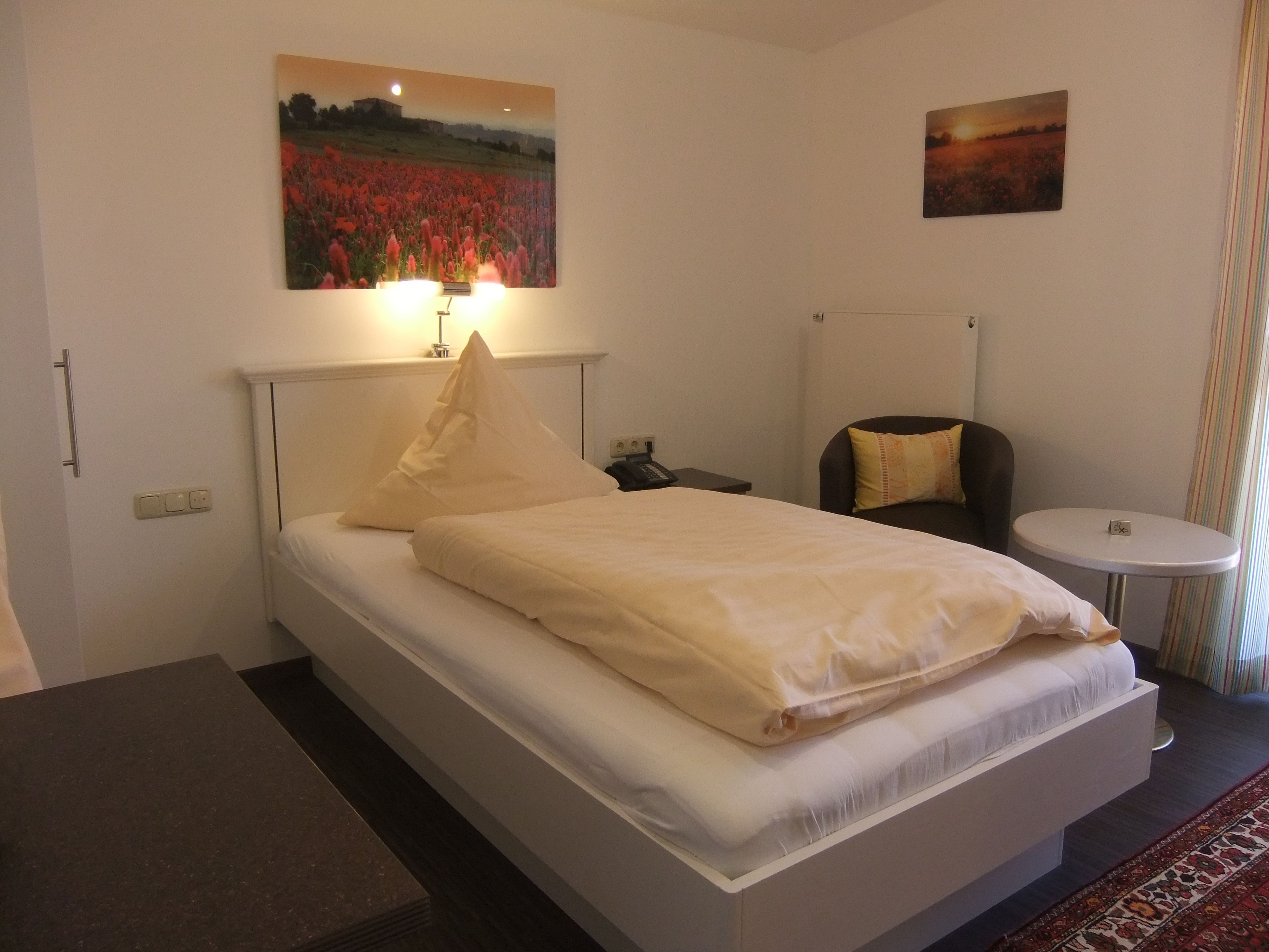 Ein Hotelzimmer mit einem Bett, einem Nachttisch, einem Sessel, einem kleinen runden Tisch und zwei Bildern an den Wänden.