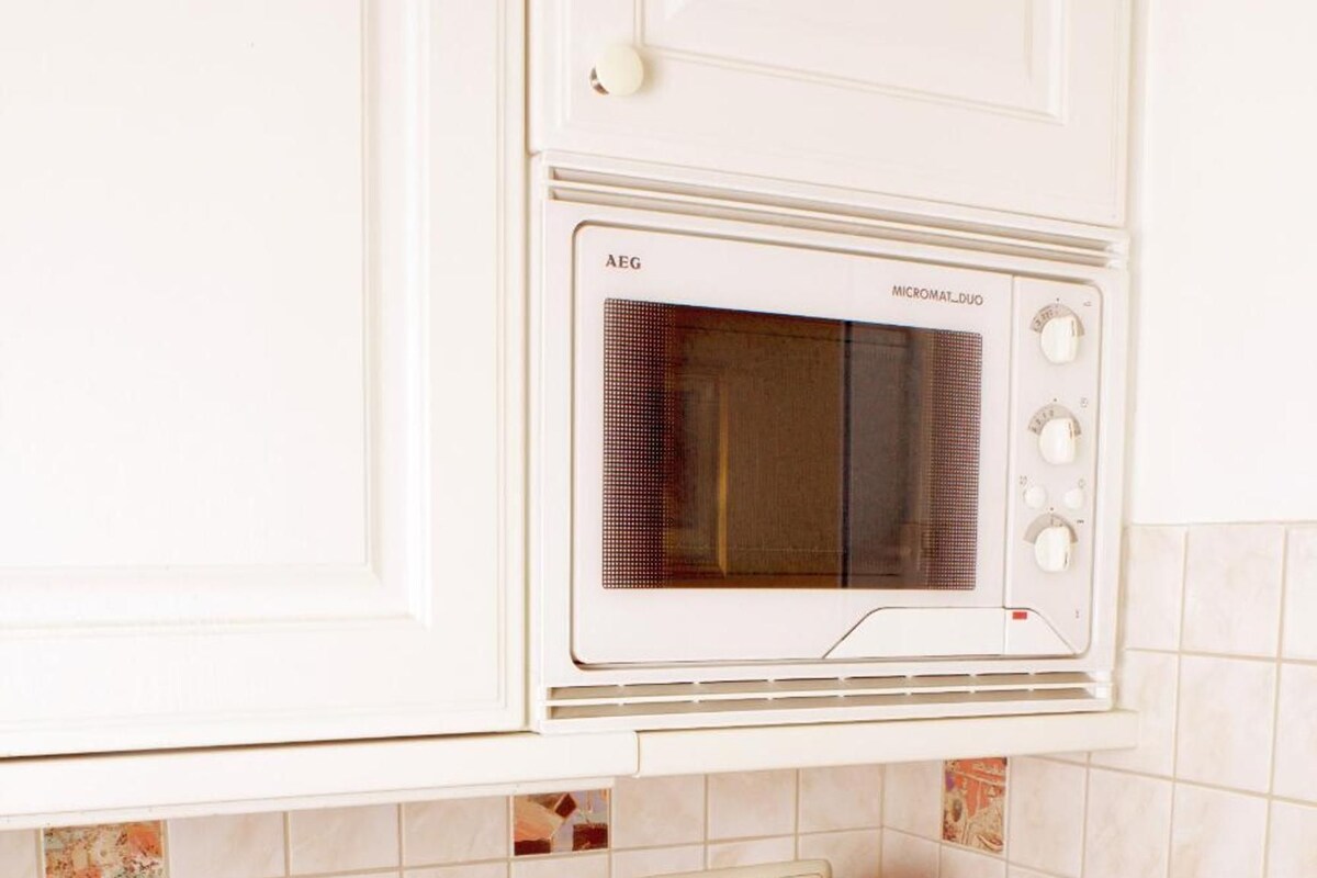 Une cuisine équipée d’un four à micro-ondes, d’une bouilloire rouge et d’une plaque de cuisson.