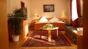 Een hotelkamer met een bed, een bank, een televisie, een tafel met bloemen en een schilderij aan de muur.