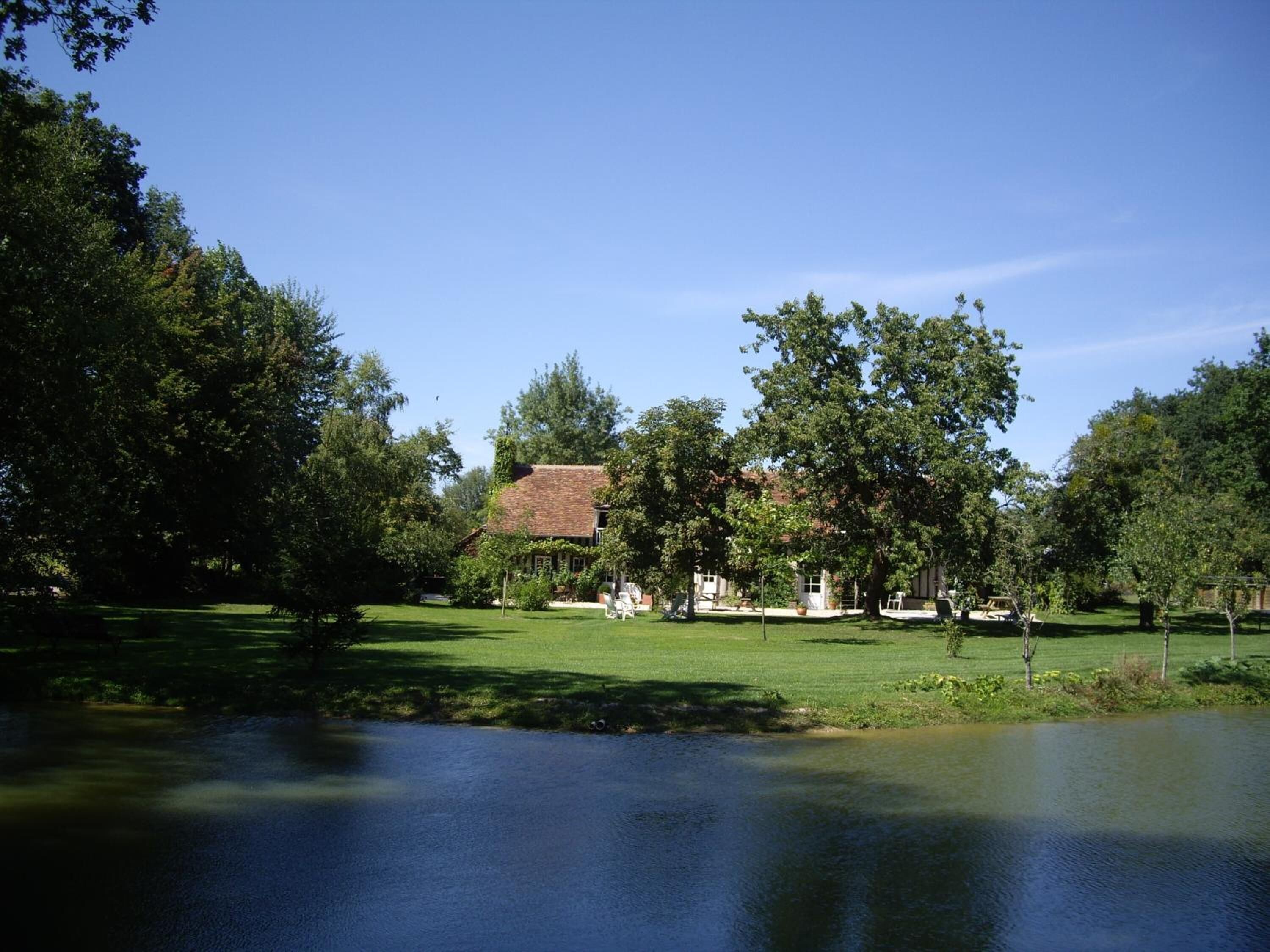 A house with a red roof surrounded by trees and a pond.