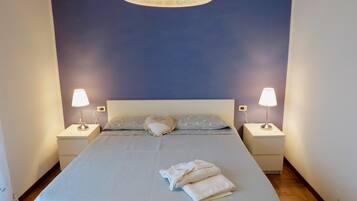 Una cama bien hecha con colcha y almohadas estampadas, dos lámparas de noche y un aplique decorativo en el techo.