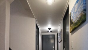 A hallway with a staircase on the left, a door at the end, and a ceiling light fixture. - Blue Mansion Guesthouse (Seoul)