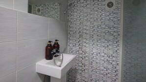 A bathroom with a white sink, two bottles of shampoo, and a shower with patterned tiles. - Blue Mansion Guesthouse (Seoul)