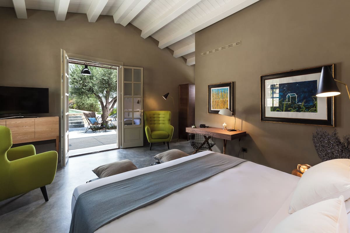 A modern bedroom with a bed, a desk, a green chair, and a TV.