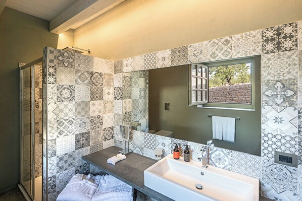 A bathroom with a large mirror, a sink, and a shower area. - Country House Villadorata (Noto)